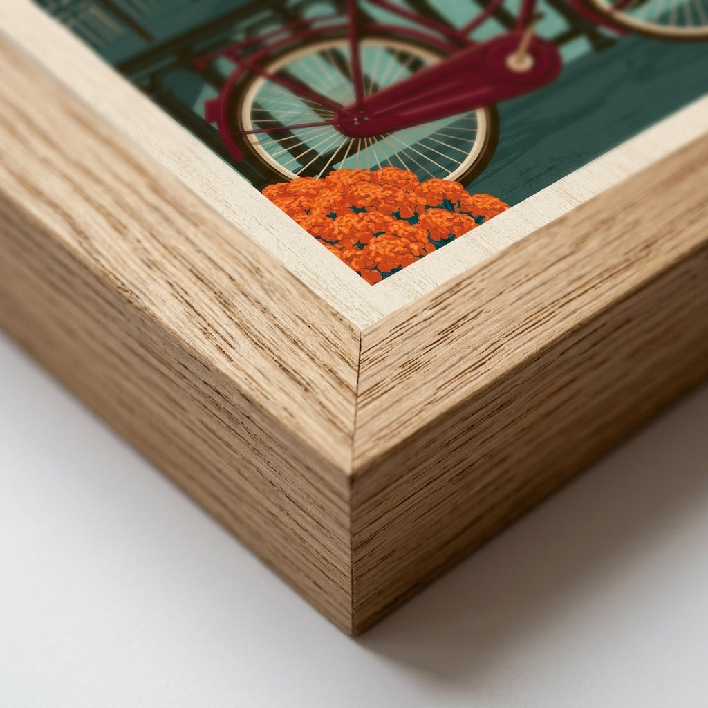 Close-up of a framed art print showing a colorful illustration of a bicycle and orange flowers, with a light natural wood frame on a white background.