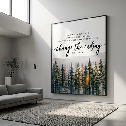 A framed wall art print hanging on a light gray wall in a modern living room. The print features a forest scene with tall dark trees and a warm glowing sun near the horizon, with the quote 'YOU CAN'T GO BACK AND CHANGE THE BEGINNING, BUT YOU CAN START WHERE YOU ARE AND change the ending' and 'C.