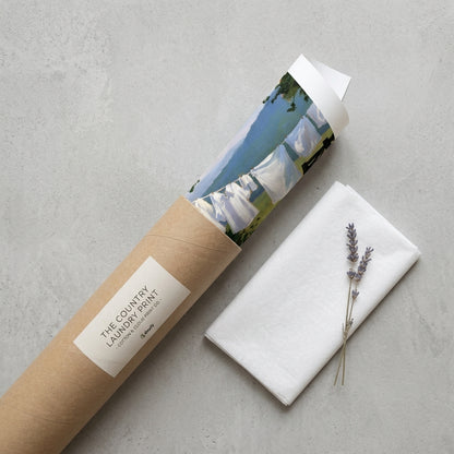 A rolled kraft-paper tube labeled 'THE COUNTRY LAUNDRY SPRIT' lies on a light gray surface beside a folded white cloth with a small sprig of lavender.