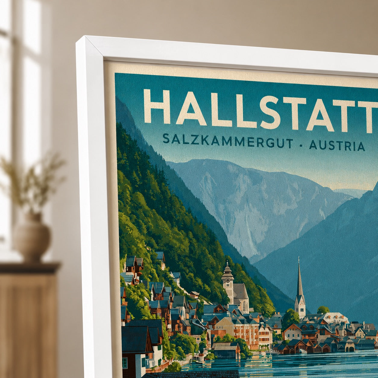A framed vintage-style travel poster of Hallstatt, Salzburgkammergut, Austria, leaning against a wall in a softly lit interior. The poster shows a mountain village by the water with green hills, blue mountains, and cream lettering.
