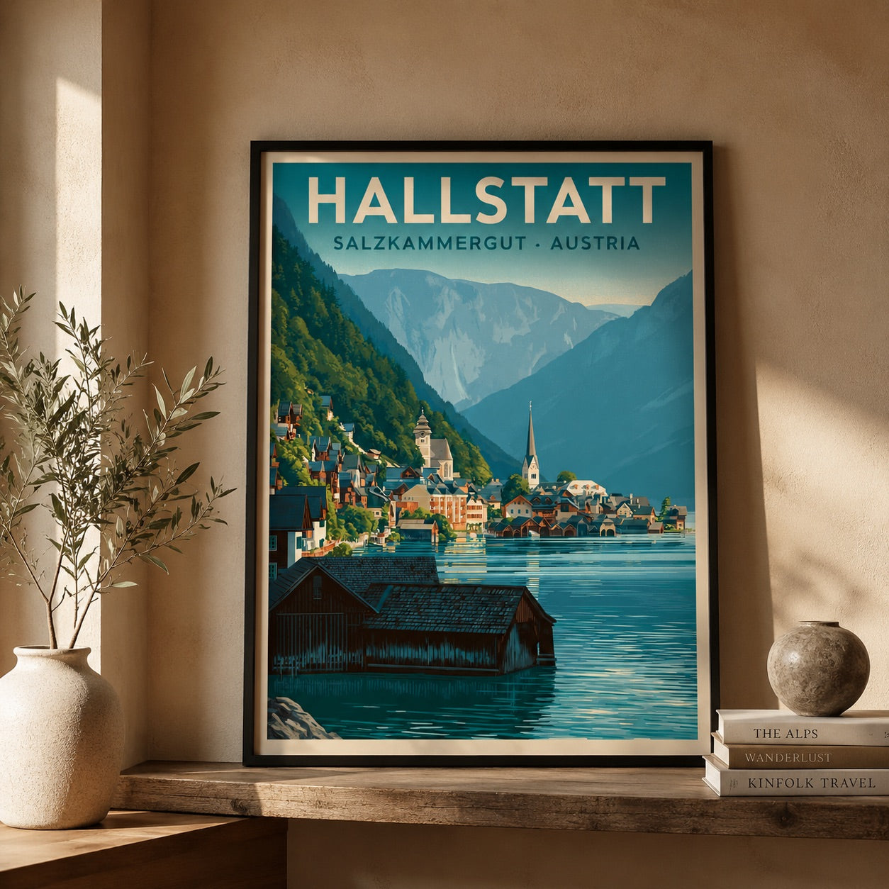 A framed travel poster of Hallstatt, Salzburg-Kammergut, Austria, leaning on a wooden shelf against a beige wall. The poster features a vintage-style illustration of the Austrian mountain town with blue water, green hills, and buildings, with 'HALLSTATT' printed at the top.