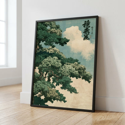 A framed art print featuring a Japanese-style tree with green foliage and white clouds against a pale blue sky, leaning against a white wall on a light wood floor.