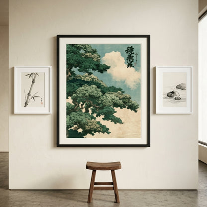 A framed Japanese-style art print depicting a green pine tree and clouds, displayed on a beige wall in a room setting with two smaller framed prints and a wooden stool below.